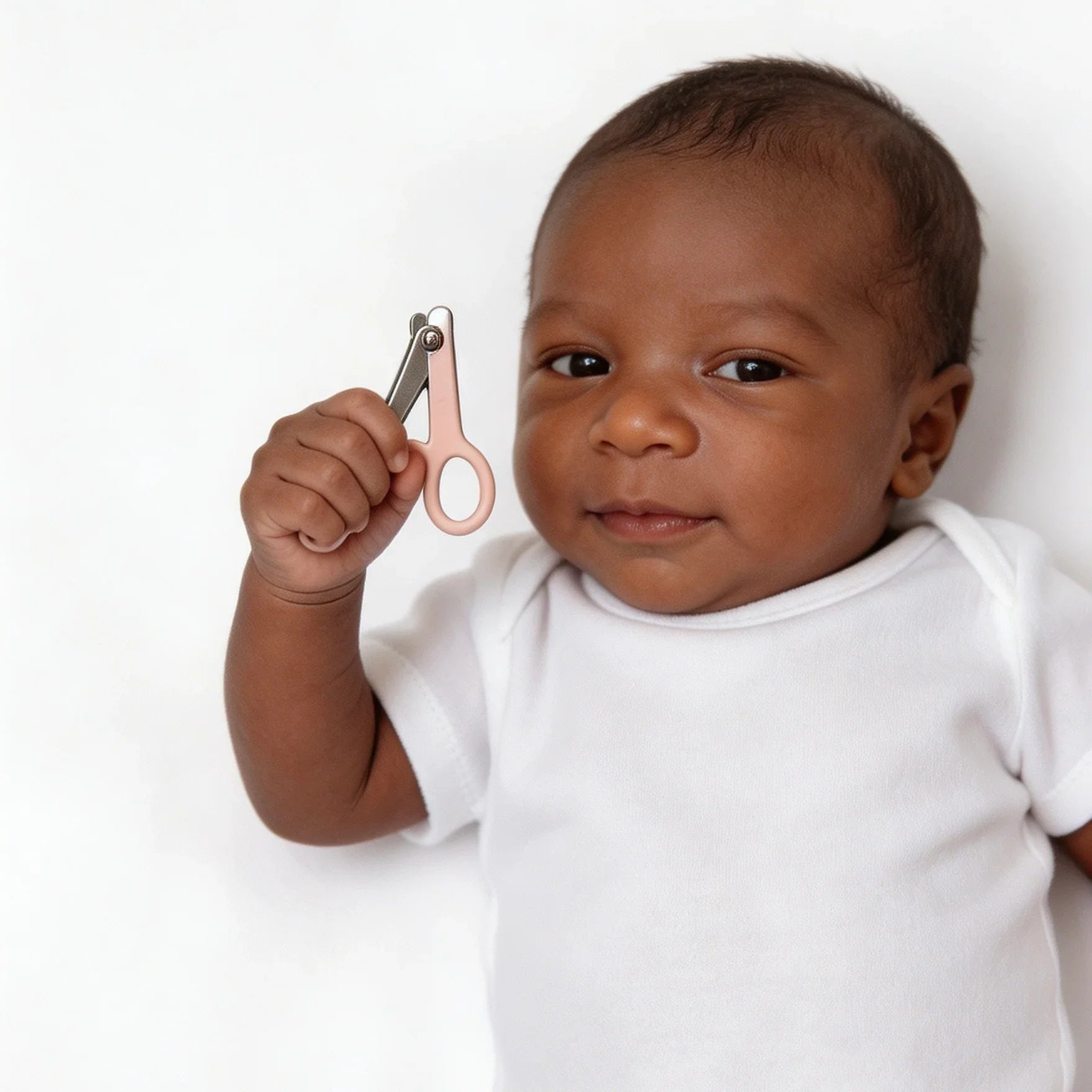 Baby in white onesie holding pink handled nail clippers against white background